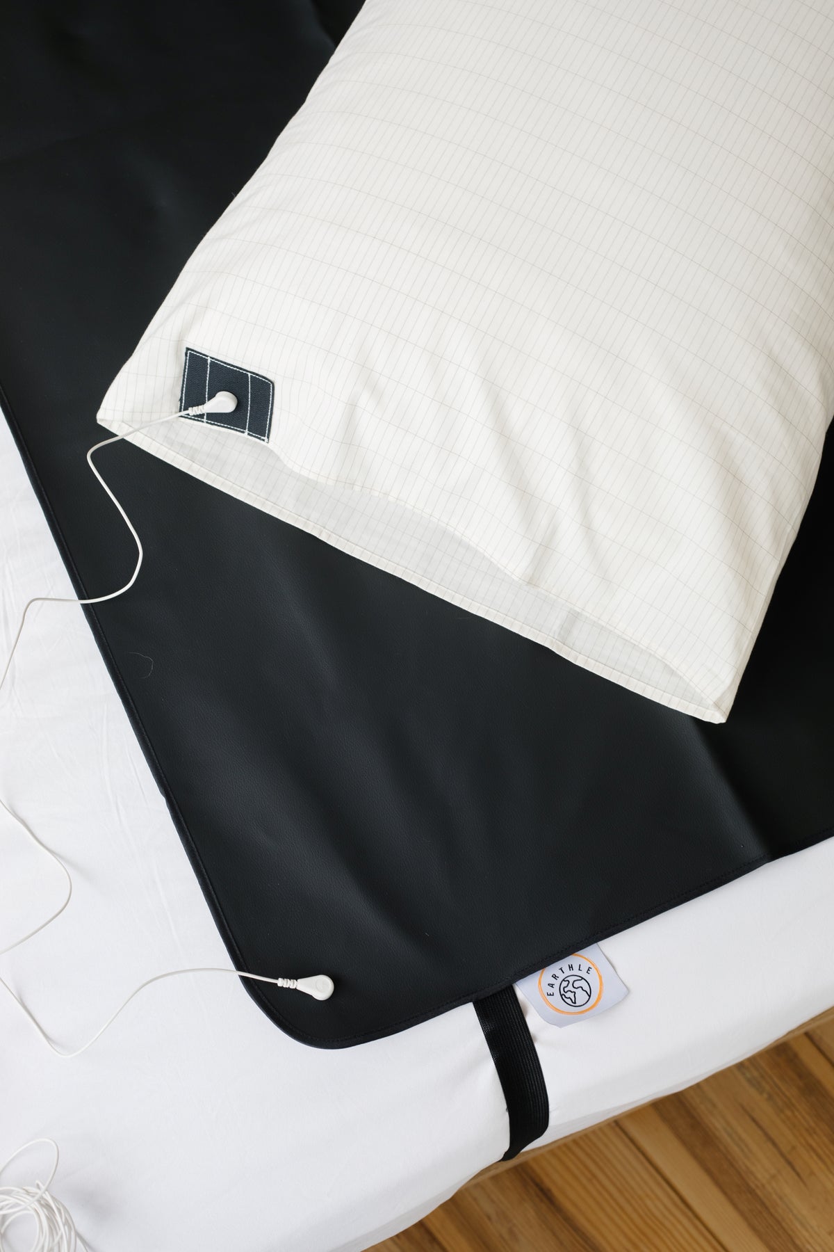 Earthle Erdungskissenbezug auf einem Bett neben der schwarzen Schlafmatte, mit dem Erdungskabel