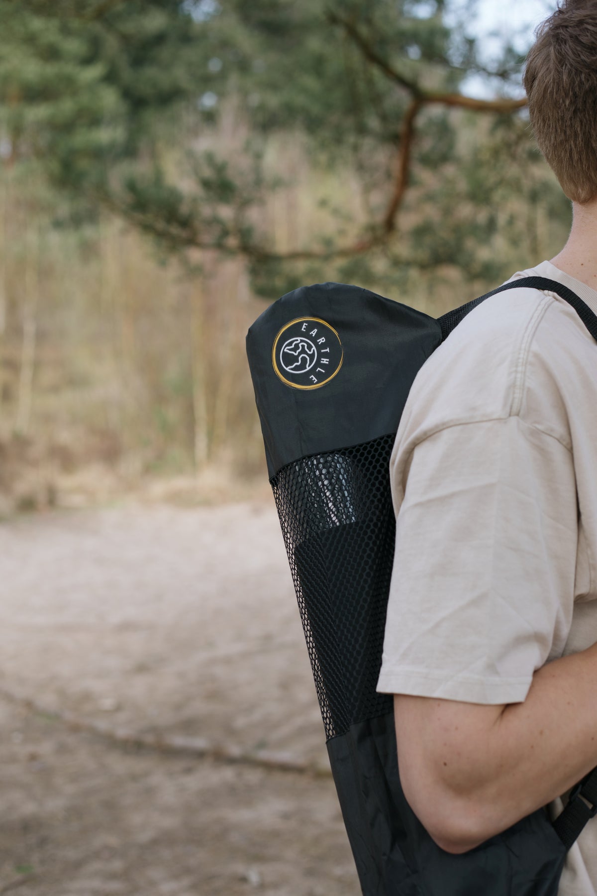 Jemand trägt die Earthle Erdungs-Yogamatte in der Tragetasche auf dem Rücken, draußen im Wald