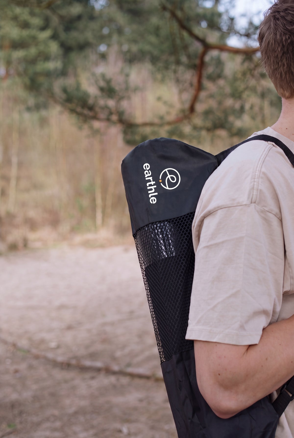 Jemand trägt die Earthle Erdungs-Yogamatte in der Tragetasche auf dem Rücken, draußen im Wald