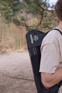 Jemand trägt die Earthle Erdungs-Yogamatte in der Tragetasche auf dem Rücken, draußen im Wald